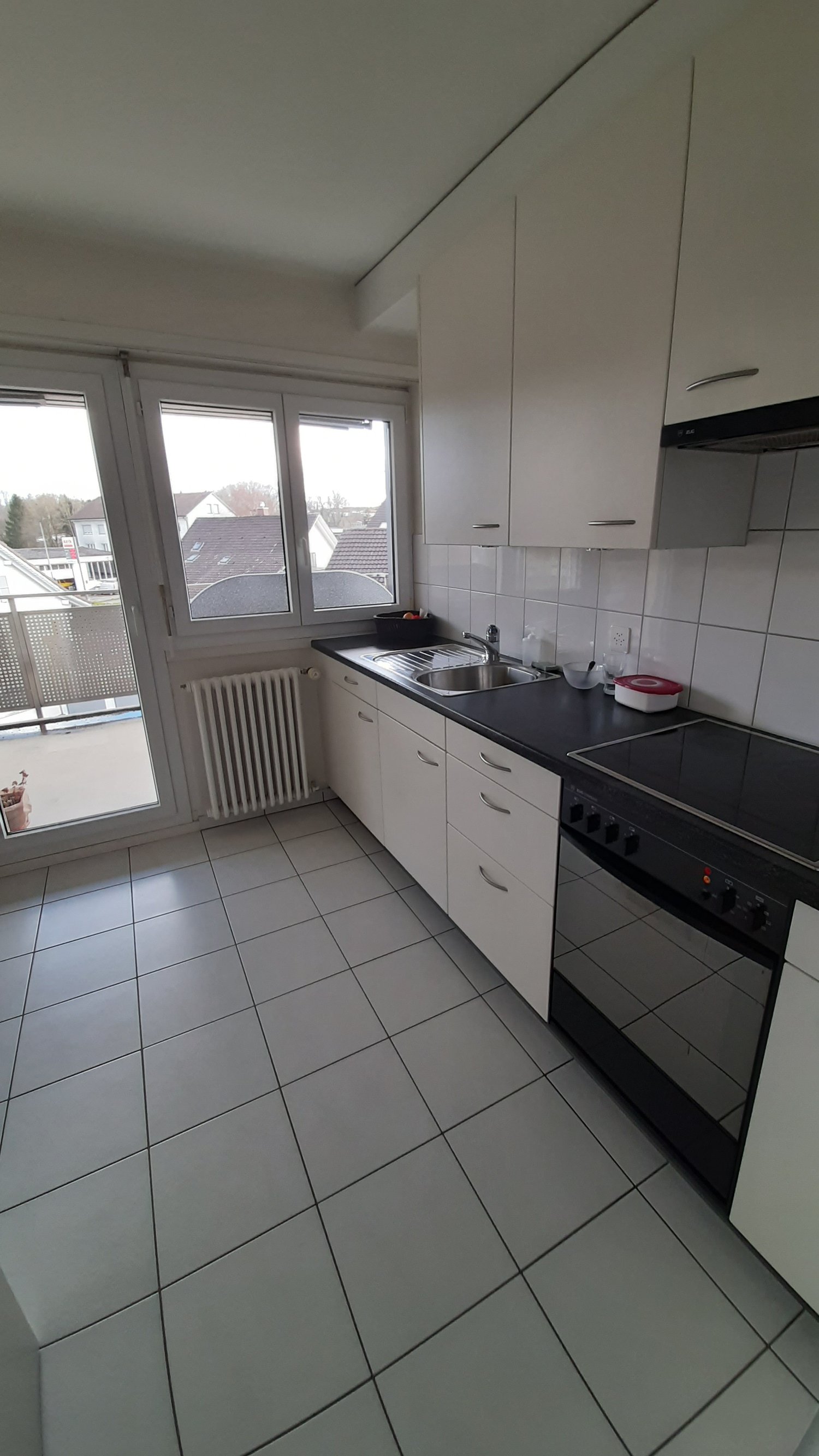 white kitchen, tiled floor, white cabinets, black countertops, windows with balcony