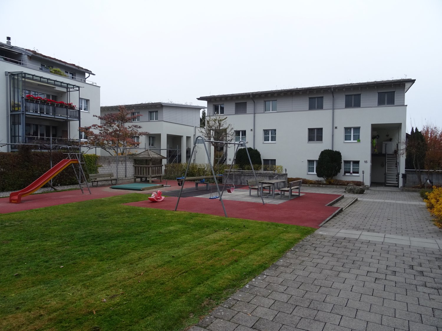 concrete floor, red floor, green grass, playground, swings, bench, slide, playground equipment, tree