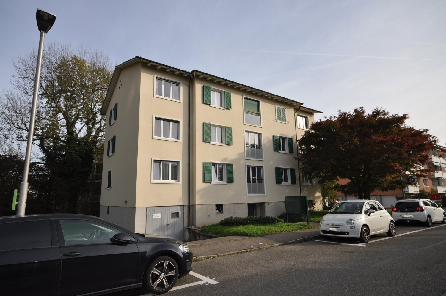 4 story apartment building, beige exterior, green shutters, multiple windows, parked cars in front