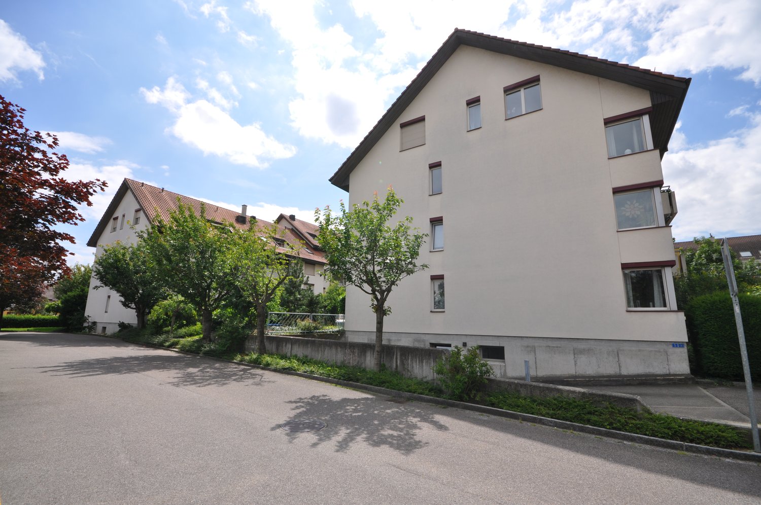 White building with multiple windows, red roof, concrete fence