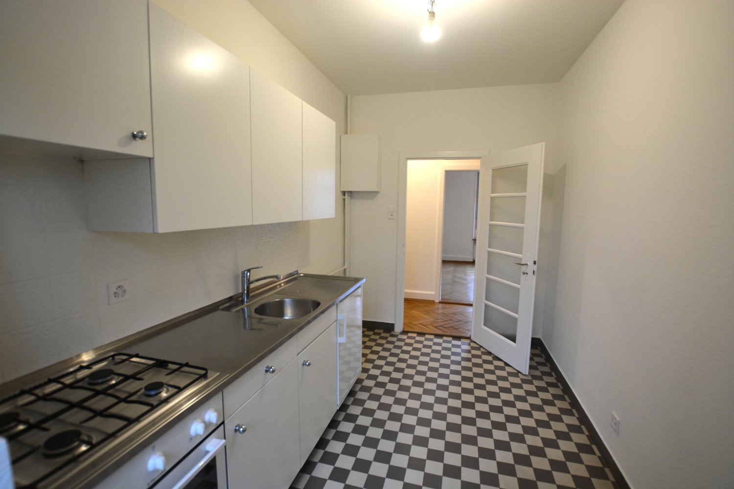 Modern kitchen with gray tiled countertop, black and white checkered floor, stainless steel sink, oven, and gas stove, and built-in cabinets