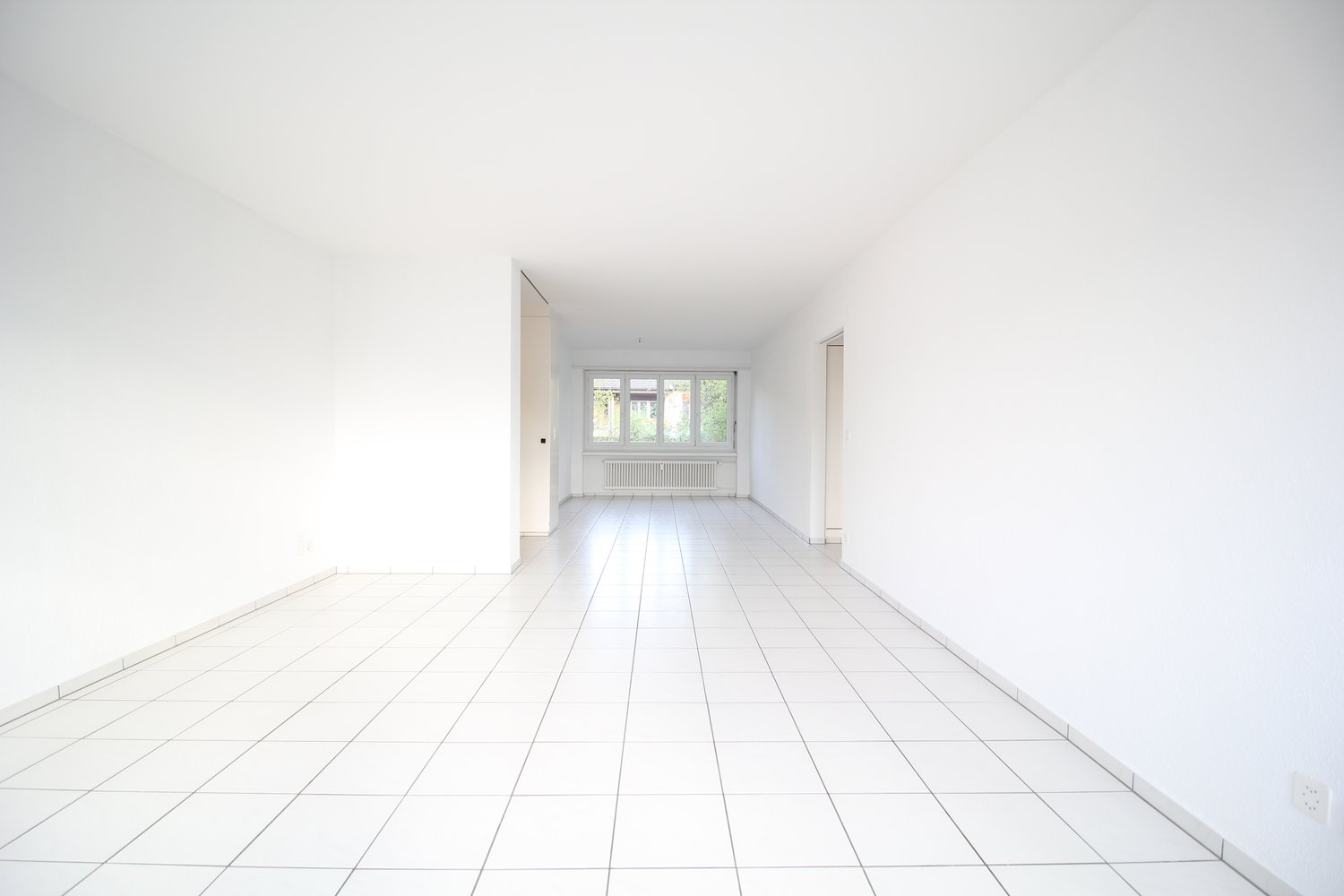 Empty room with white walls and floor, two doors, window with white radiator