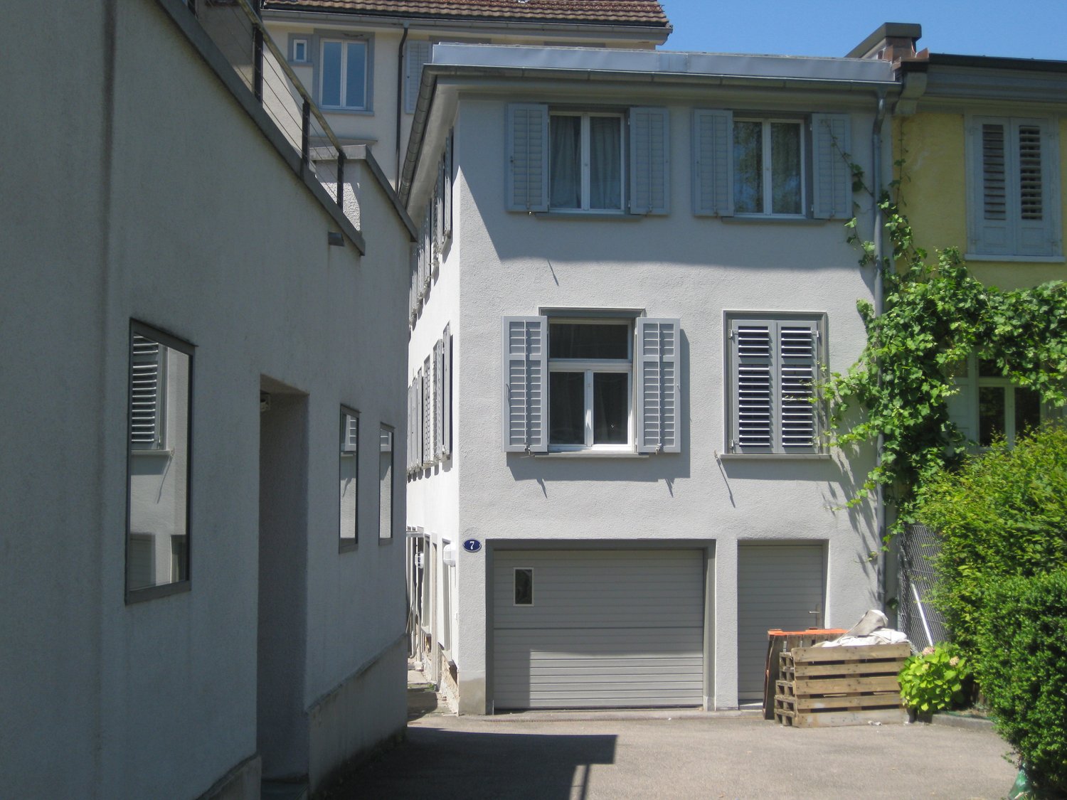 Two-story residential building with white exterior, several windows with shutters, two garages, and a small garden