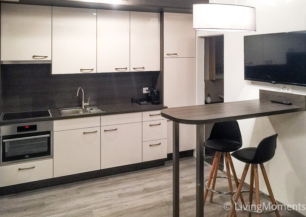 White cabinetry, black granite countertops, integrated appliances, open shelving, black barstools, stainless steel oven and microwave, flatscreen TV