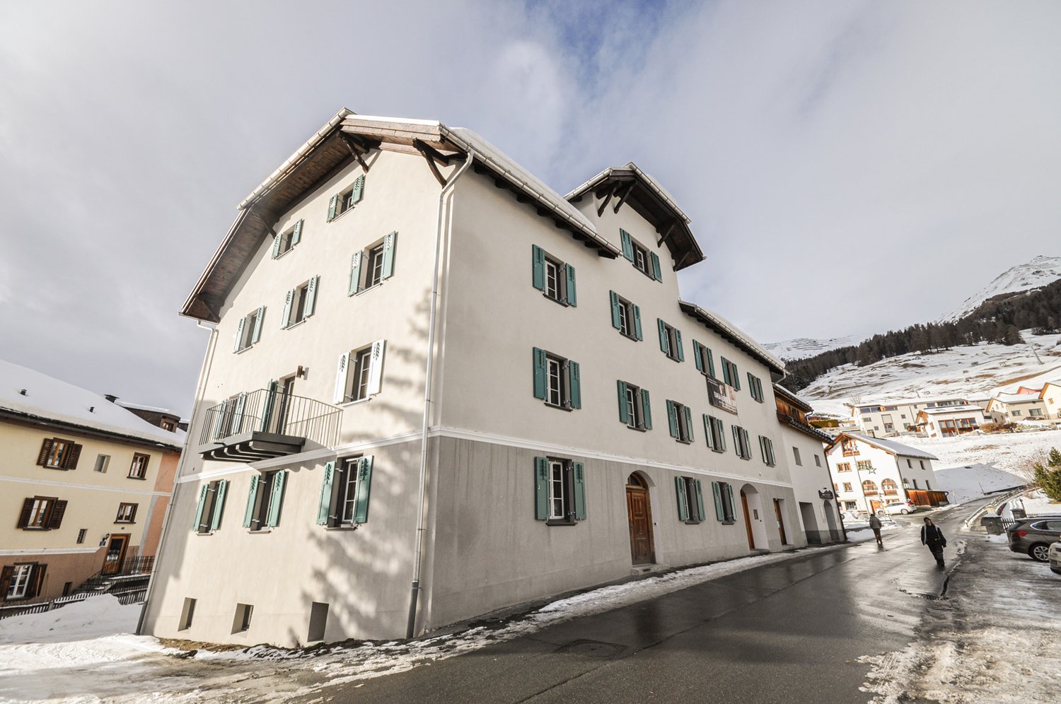 3 story white building, snow on roof, wooden balconies, wooden front door, snowy street, snow on ground