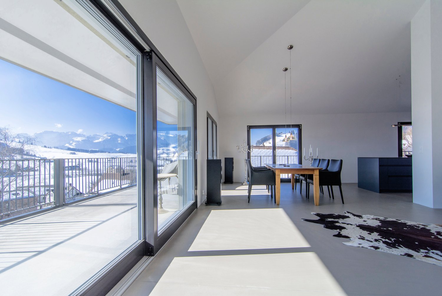 large windows, balcony, wooden floor, dining area with dining table and chairs, black cowhide rug