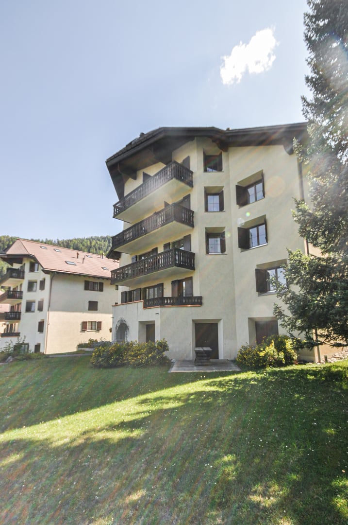 White facade, multiple balconies, elevated terrain, multiple floors, mountain backdrop