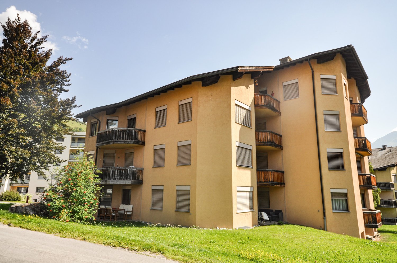 Three story yellow building, modern design, multiple balconies with tables and chairs