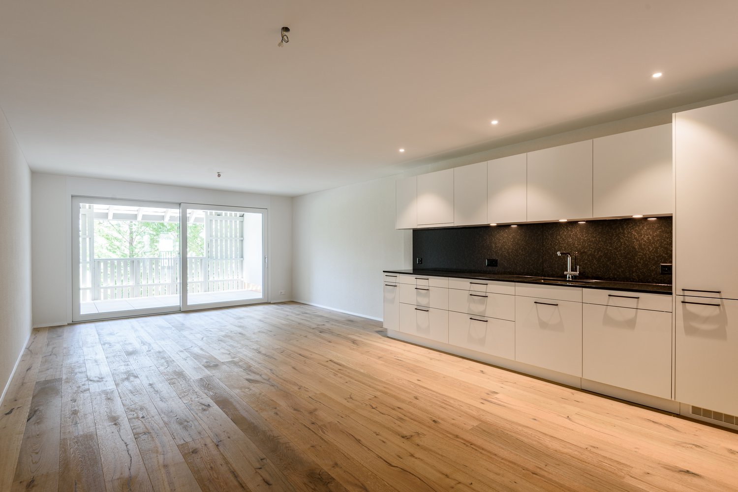 kitchen with sliding doors, balcony, wooden floor, white cabinetry, modern sink