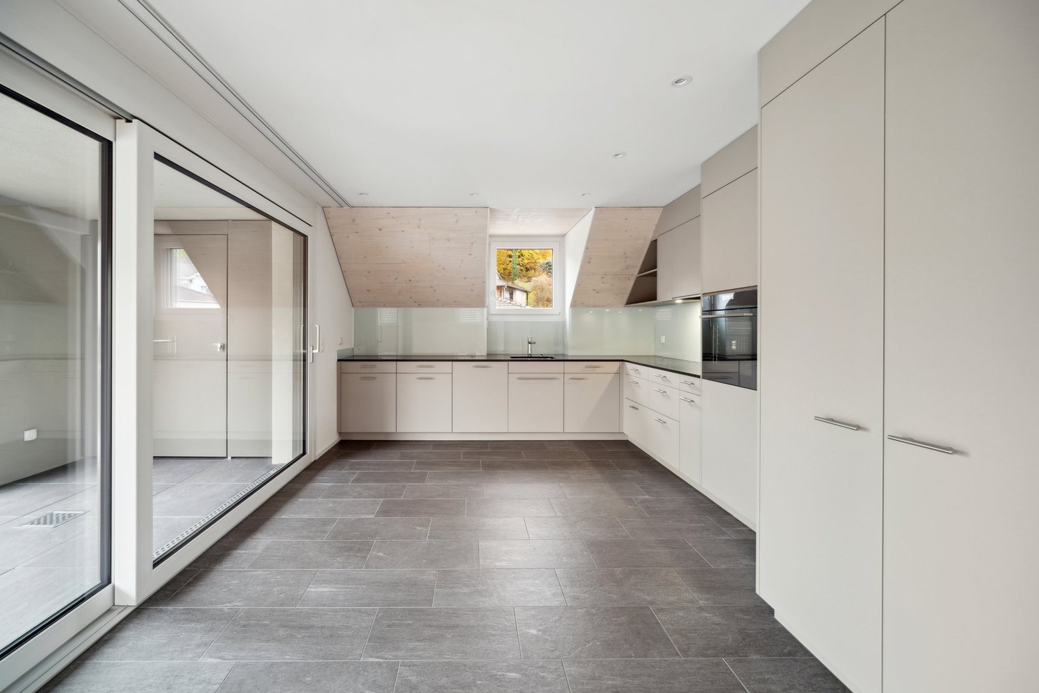 white cabinets, black countertop, white tiled flooring, glass doors and windows, small kitchen island with sink and faucet