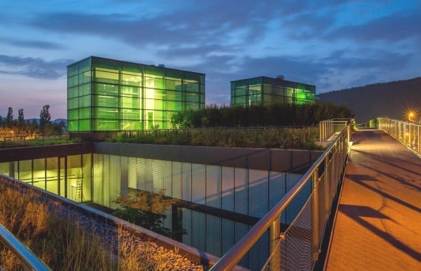 modern building with green glass walls, raised ground floor, metal railings, green roof