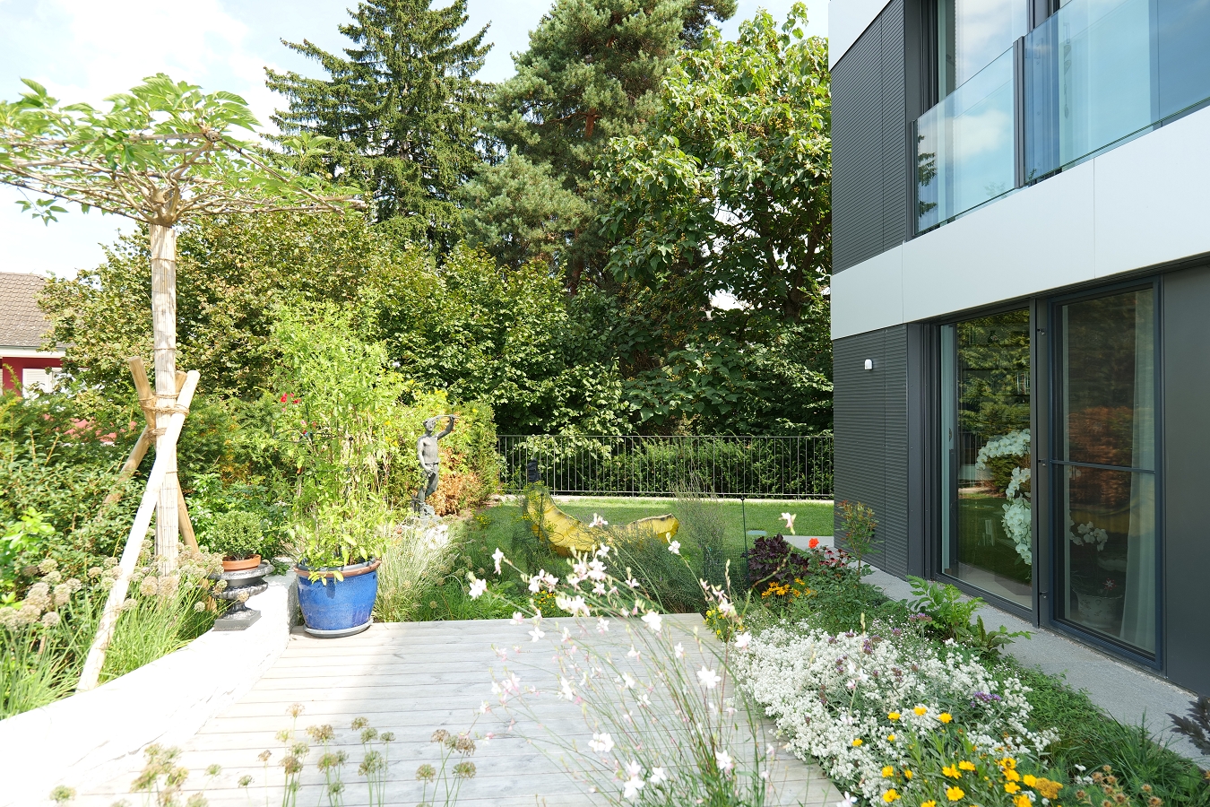 backyard, flower garden, wooden pathway, garden fence, plants, potted plants, statue, building with glass wall