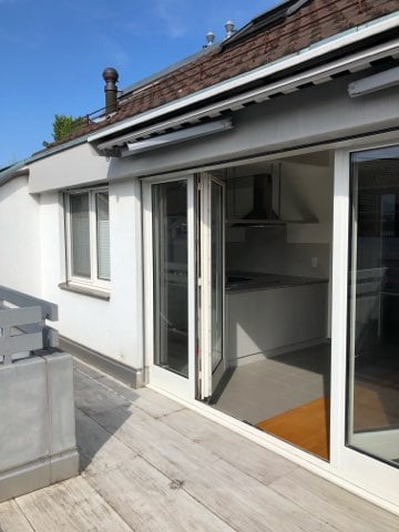 Single-story house with a wooden roof, white exterior walls, and large sliding glass doors leading to a wooden deck or balcony.