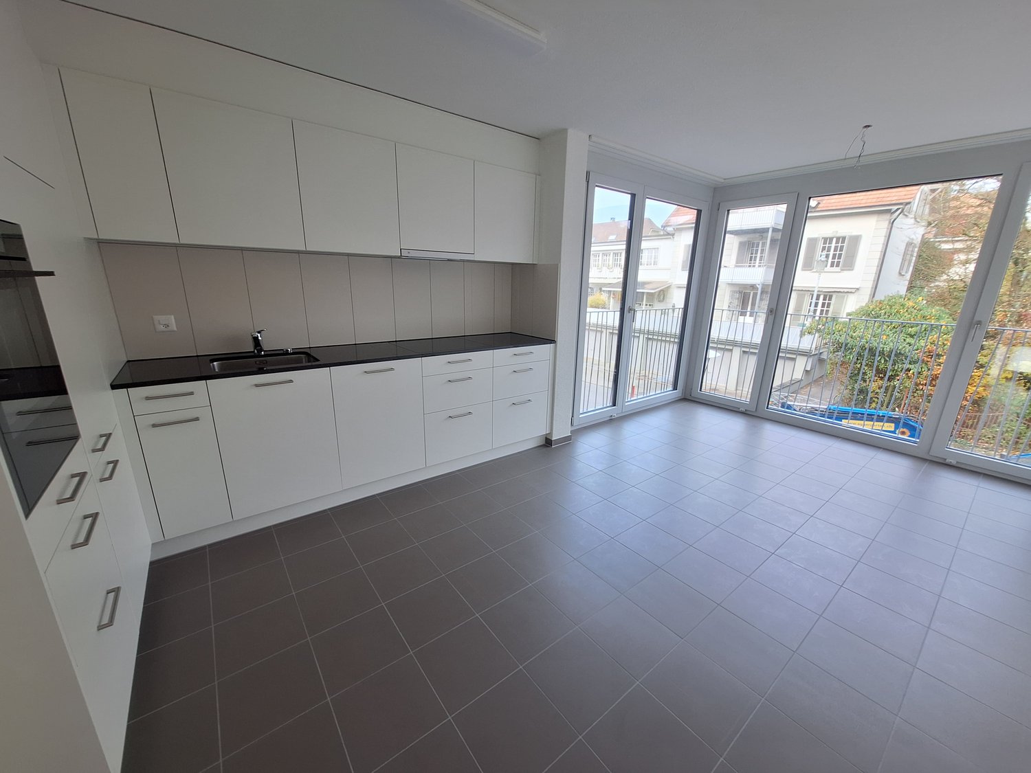 White cabinets, black countertops, stainless steel sink, tiled floor, sliding glass doors leading to balcony