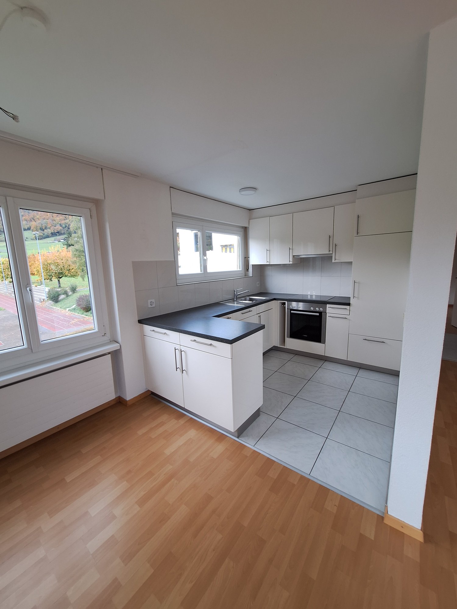 Kitchen: white cabinetry, black countertops, under-mounted sink, stove, oven, open layout, hardwood floors, windows