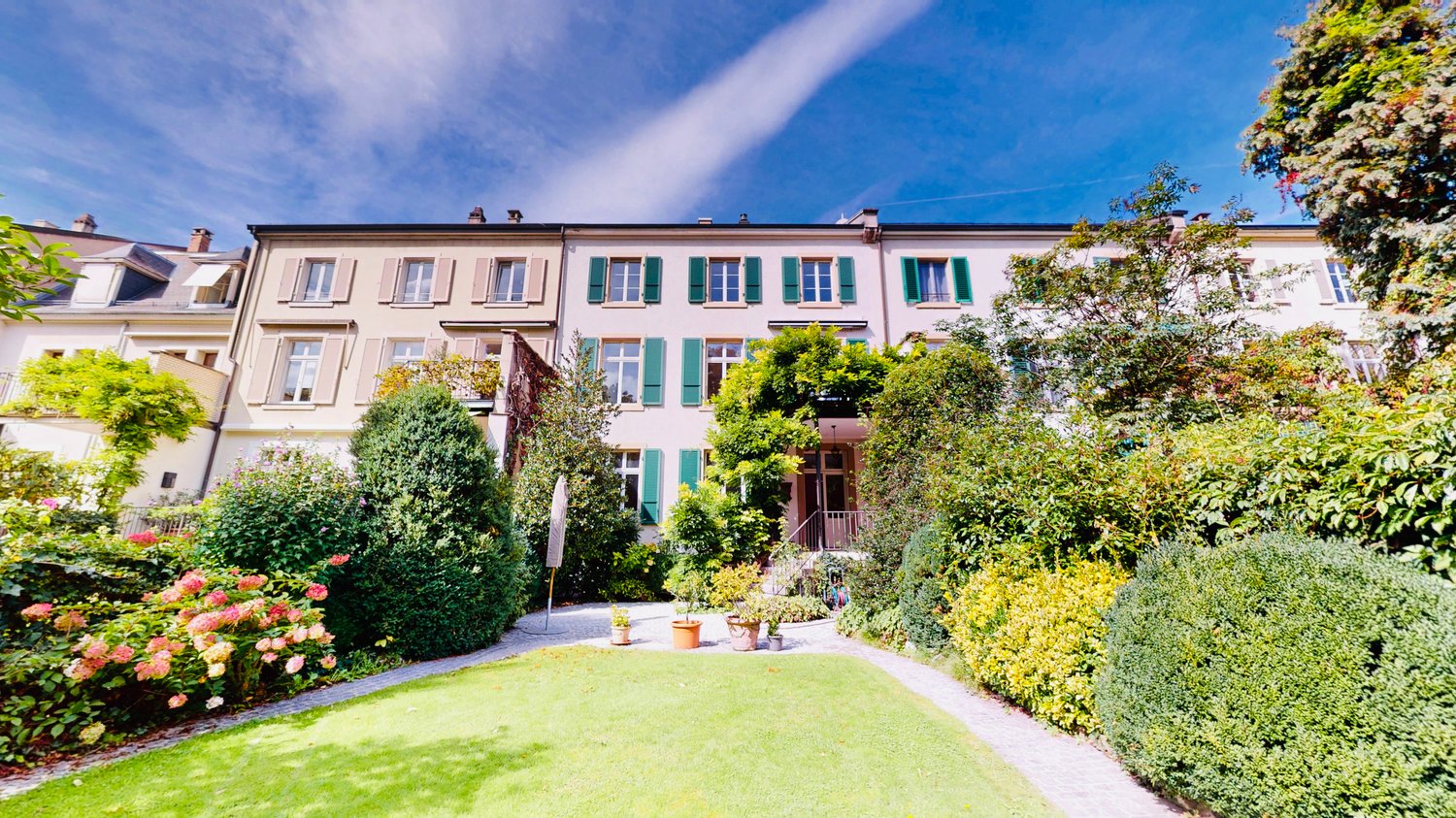 a pathway to the front entrance of the building surrounded by plants and bushes, some plants and trees in the yard