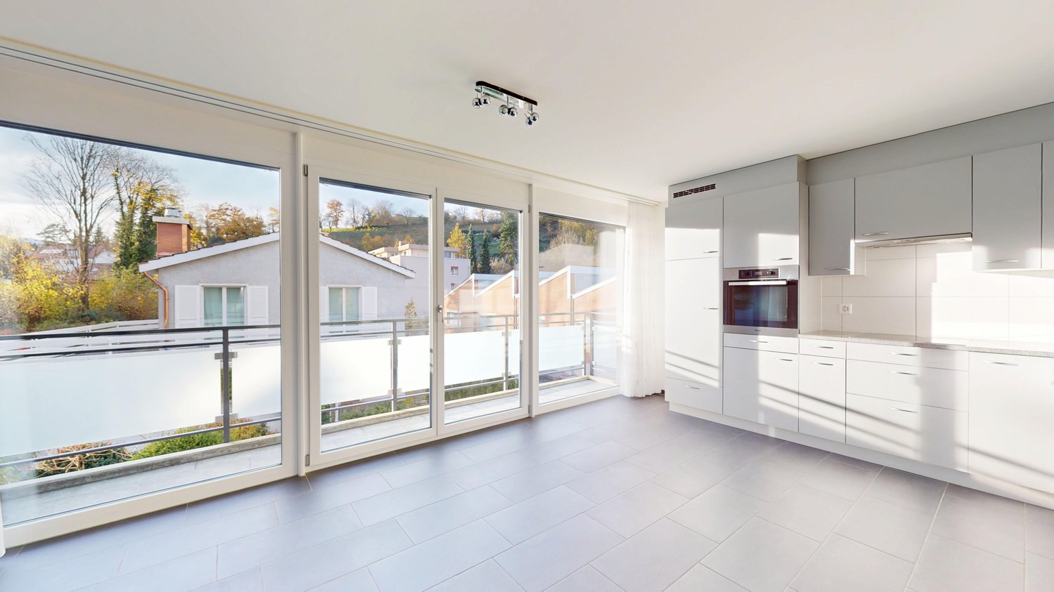 White tiles, white kitchen cabinets, oven, balcony with metal railings, sliding glass doors