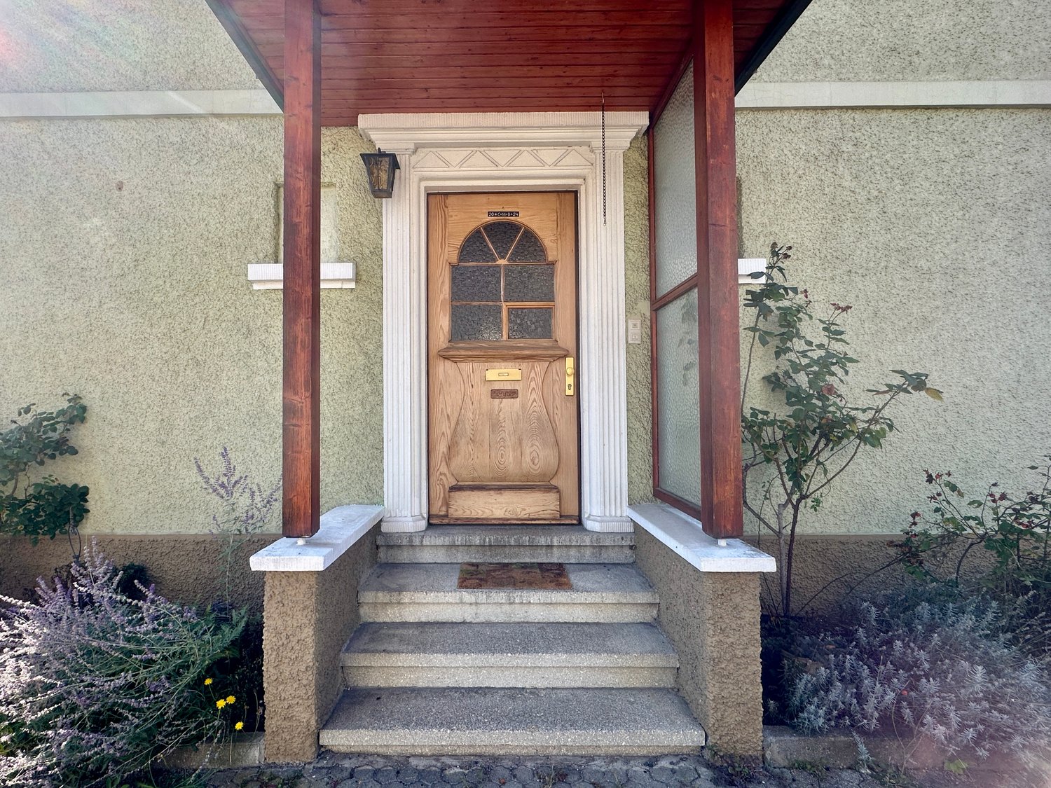 Wooden entrance door with glass windows, wooden pillars, stone stairs, plants