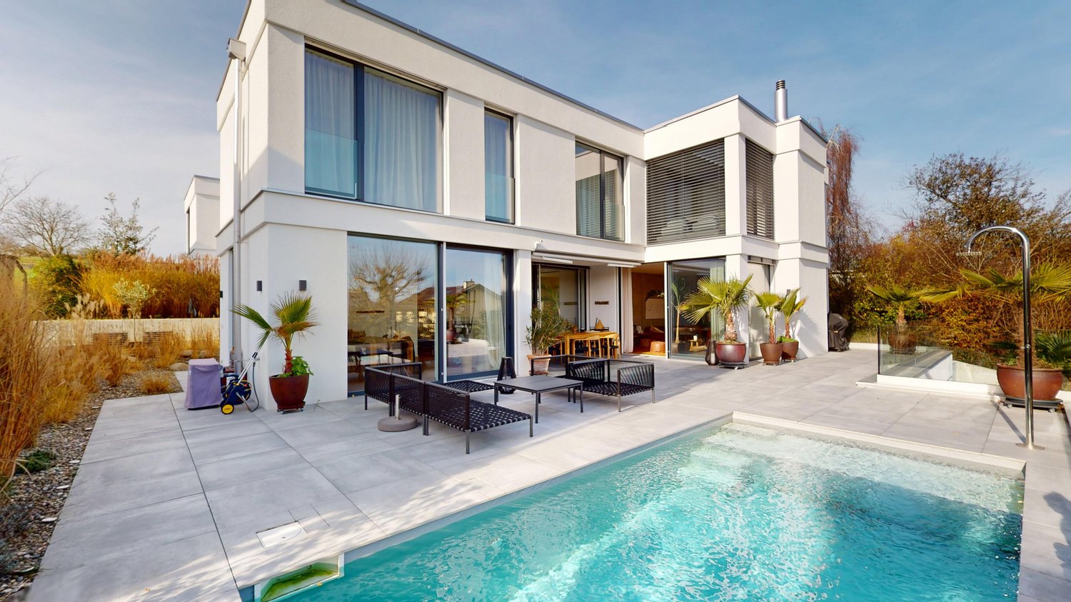 Modern white house, two stories, large windows, pool, outdoor seating area, potted plants