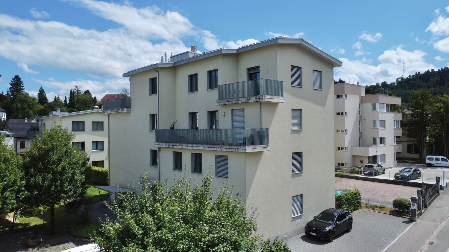 3 story building, beige exterior, multiple balconies, parking area, trees, shrubs