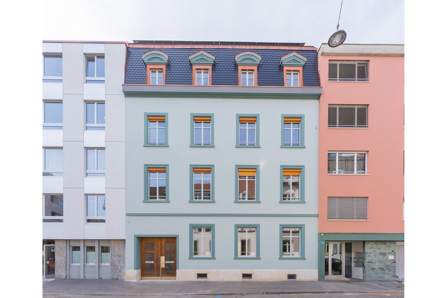 Three story building, multiple windows, blue roof, brown entrance door