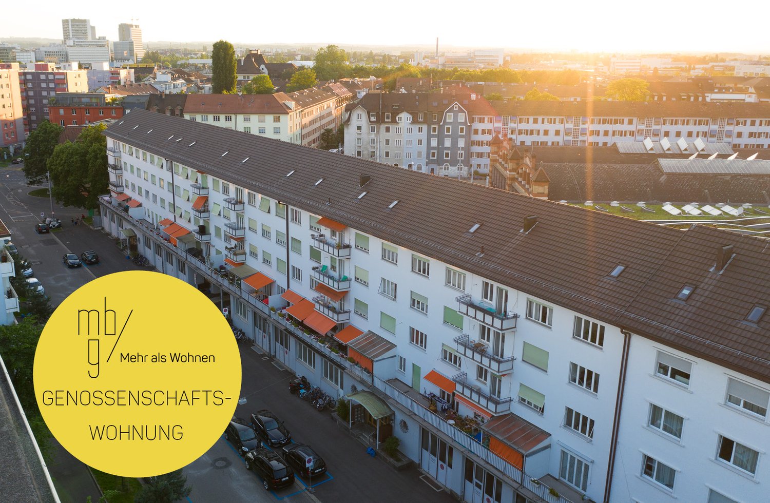 Multi-story building with balconies, brown roof, white walls, many windows, car parking