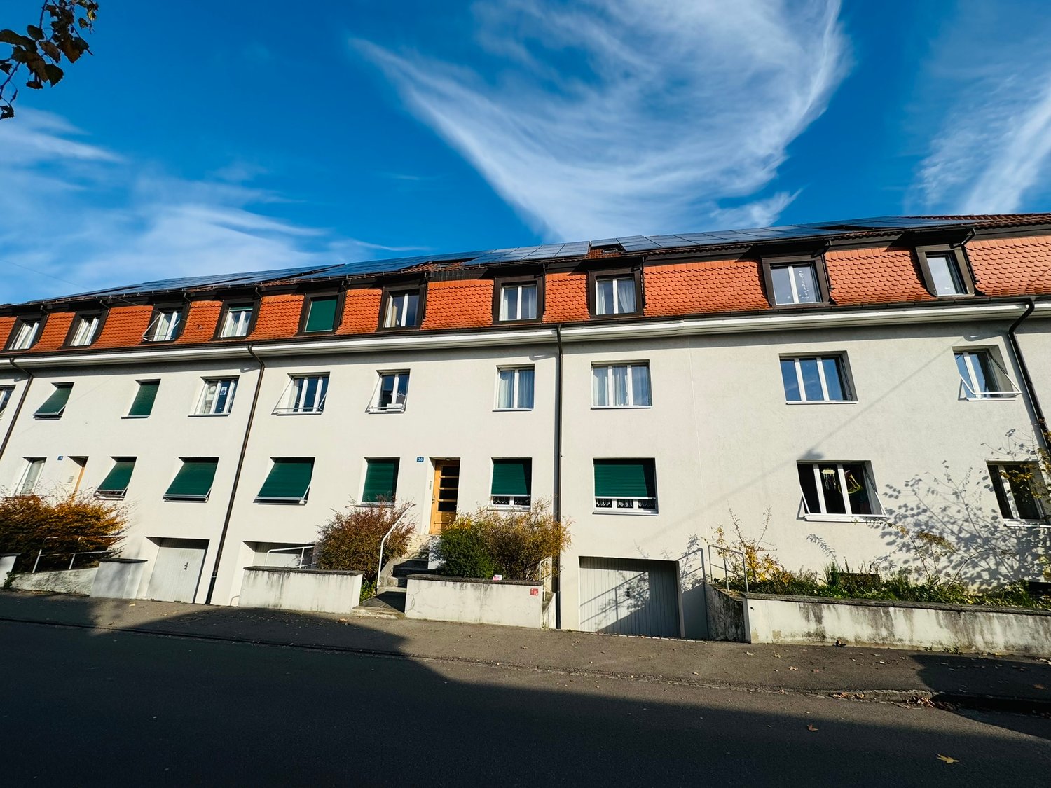 white building, raised ground floor, orange roof, solar panels, many windows, green shutters