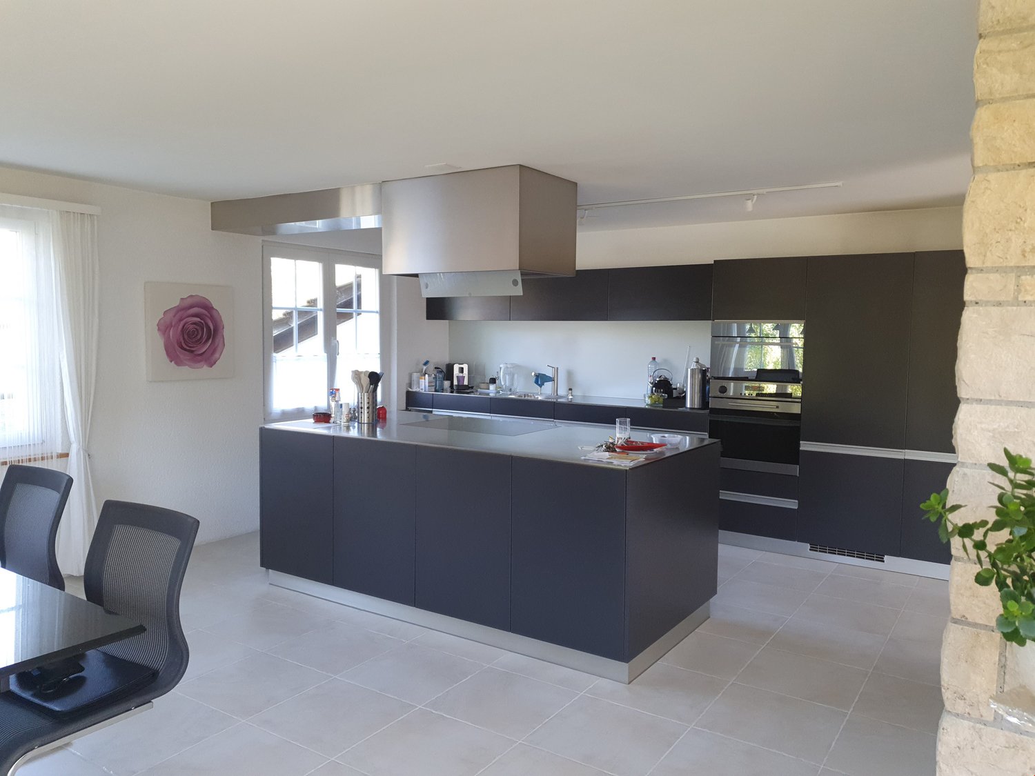 modern kitchen with black cabinets, stainless steel island, built-in oven and extractor hood, white tiled floor