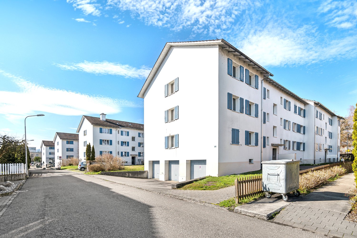 Multiple white apartment buildings, each with blue shutters, two visible garages