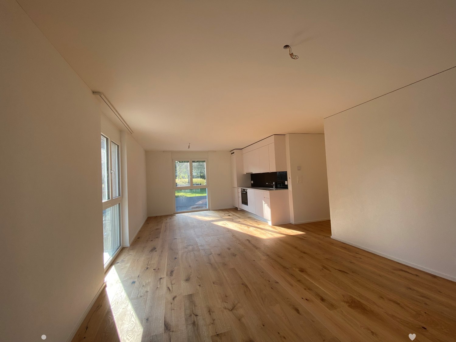 Empty room, wooden floor, white walls, windows, open to the kitchen