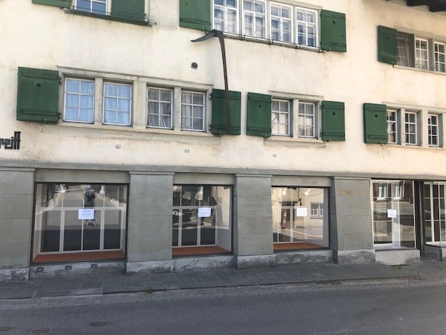 Storefront with green shutters, several windows, ground floor, two floors, sign on the left, three glass doors in front