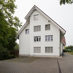 two-story house, white exterior, brick-tiled roof, brick driveway, large windows, multiple parking spaces