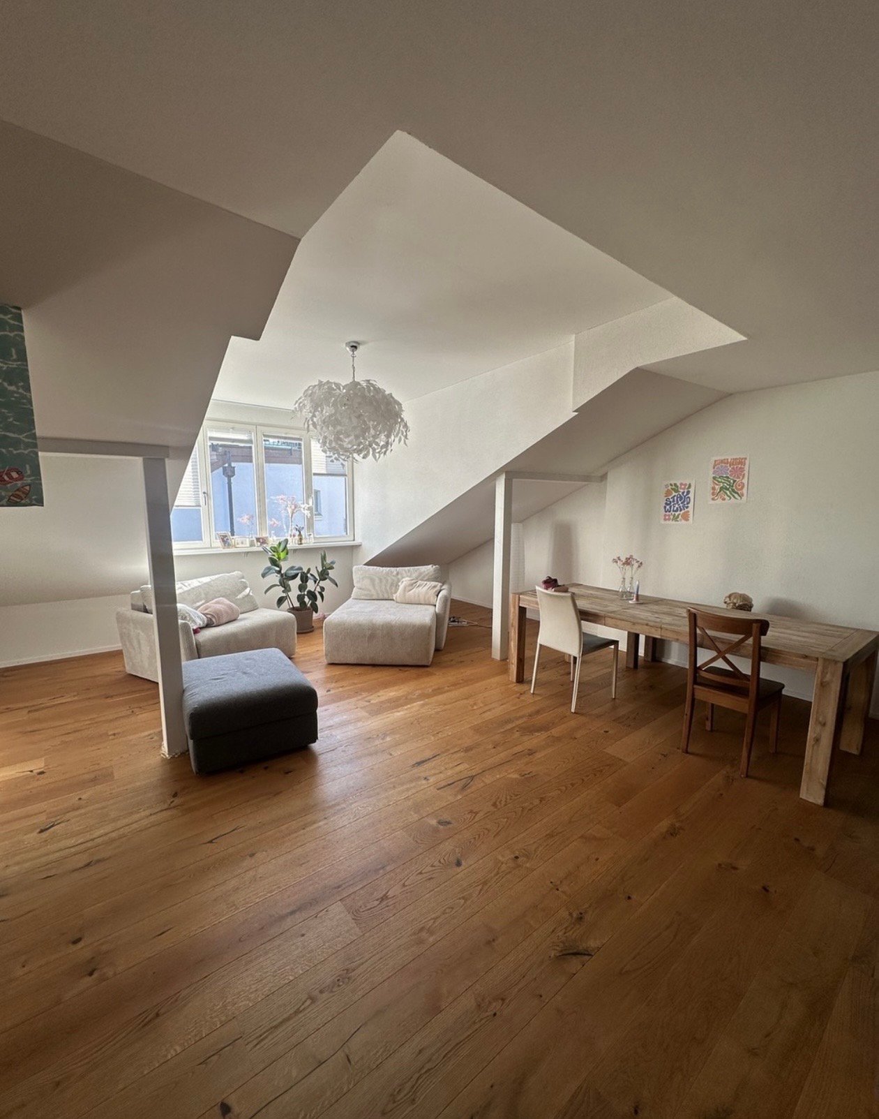 open space with wooden floor, white walls, large windows, dining table, chairs, sofa, ottoman, potted plant, chandelier
