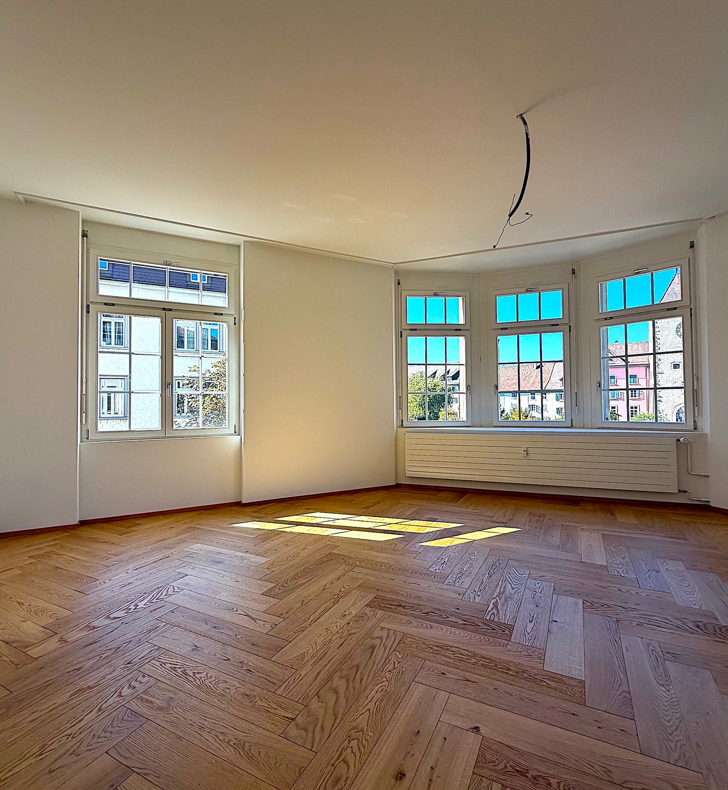 empty room, wooden parquet flooring, large windows, high ceiling, yellow sun rays