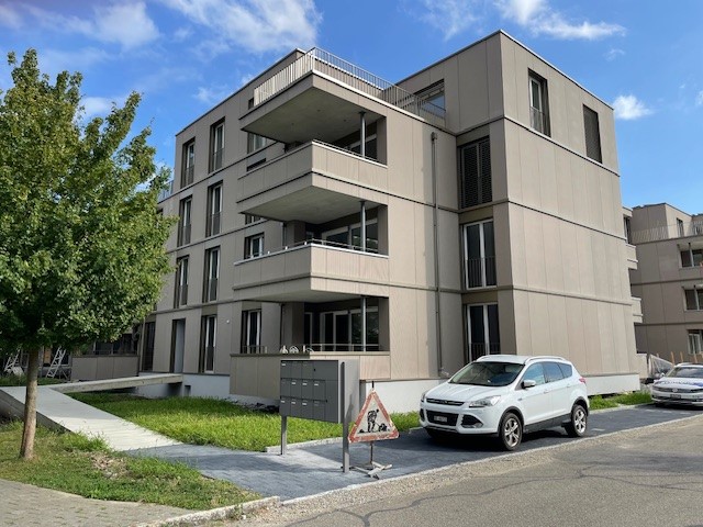 4-story modern apartment building with balconies, parking spaces in front, and surrounded by trees