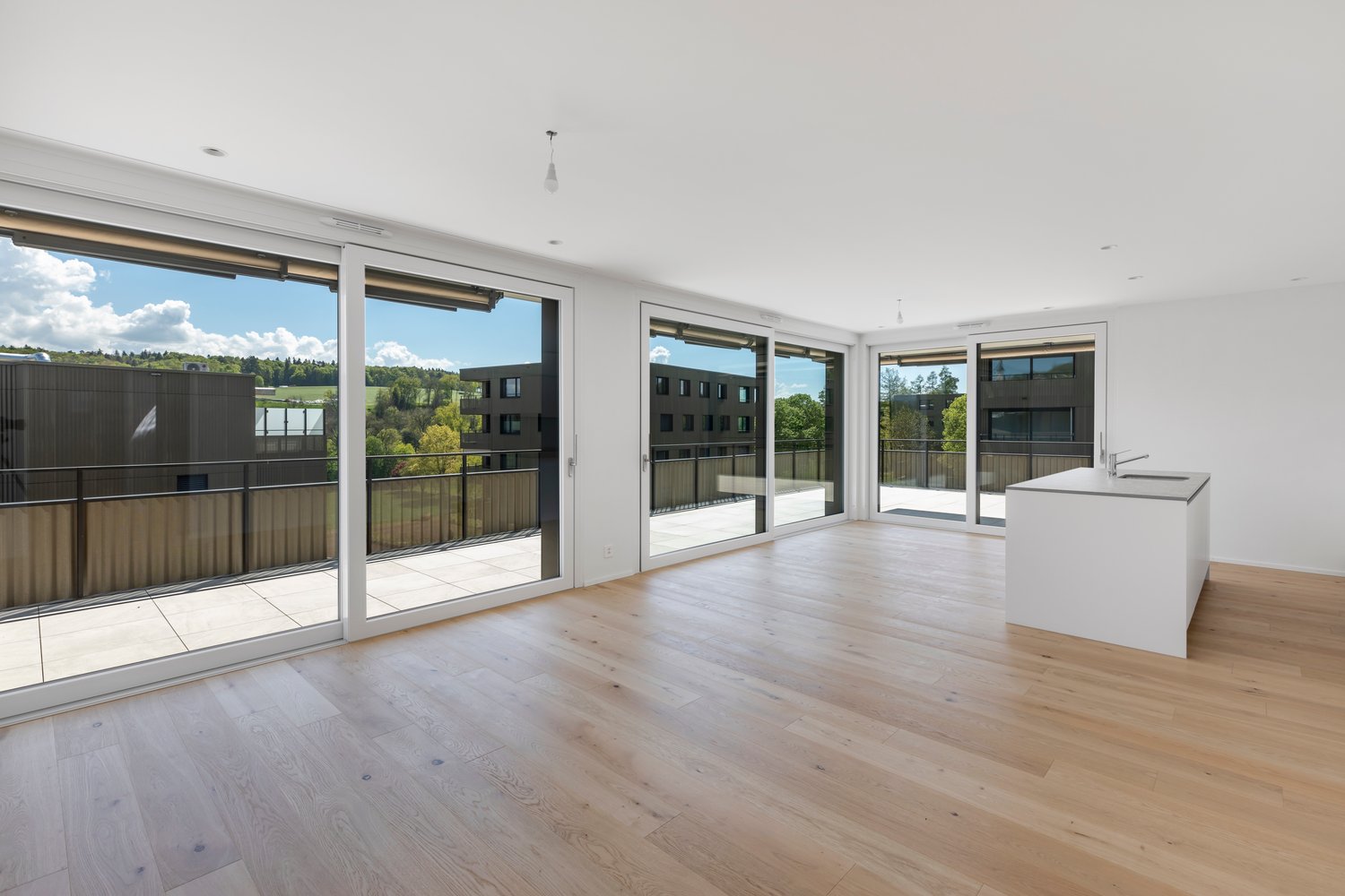 Spacious open-plan living area with large windows and sliding glass doors leading to a balcony, hardwood flooring, and a kitchen island.