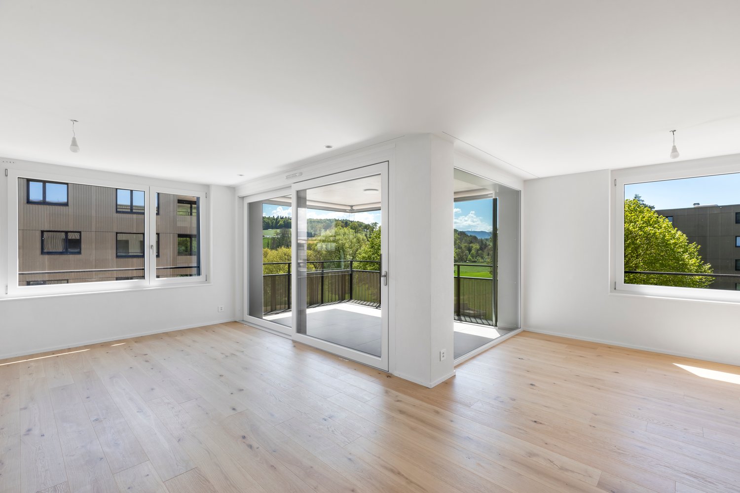 Open floor plan, wooden flooring, large windows, sliding glass doors, balcony with railing