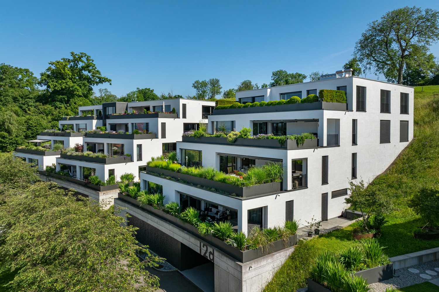 Modern apartment building with multiple levels, green rooftops, balconies and glass windows.