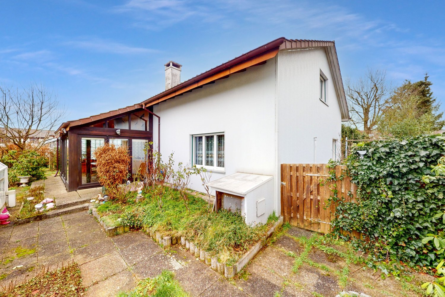 Detached white house with brown roof, glass door, two windows, chimney, wooden fence, garden, and chimney