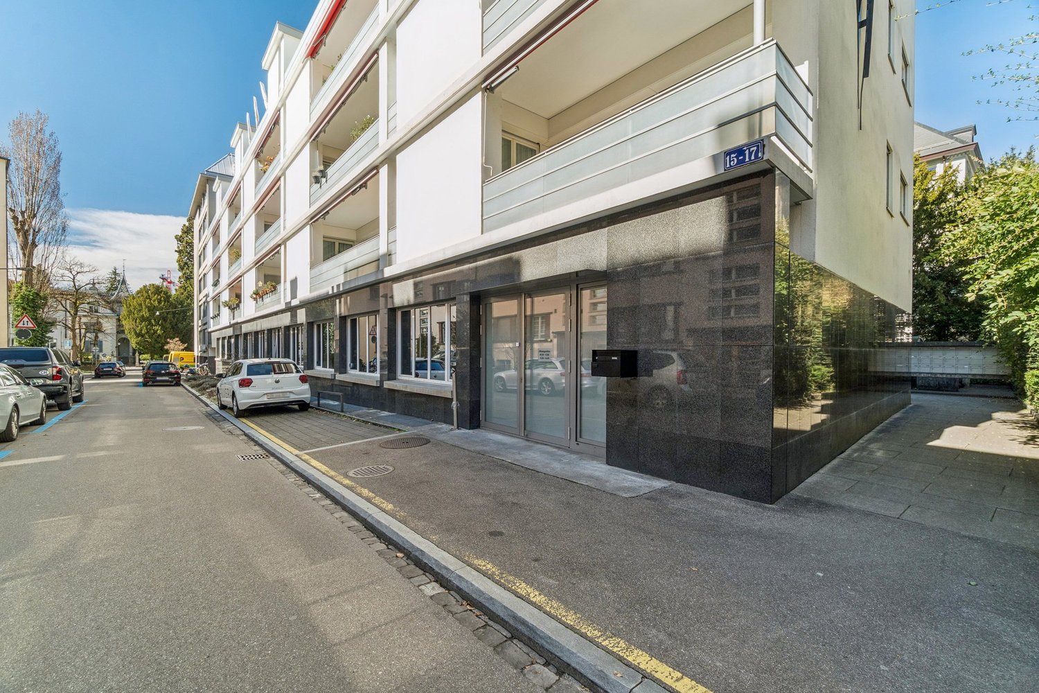 Modern apartment building, white exterior, glass doors, balconies, multiple windows, street view