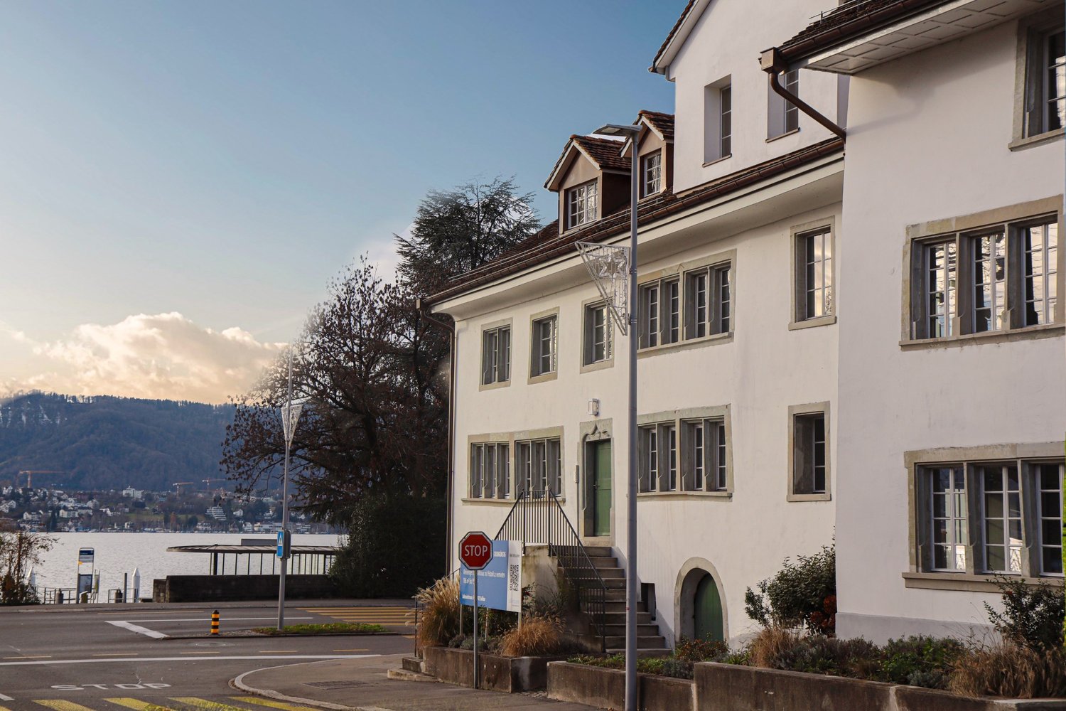 white building, multiple windows, brown roof, stop sign, lake view