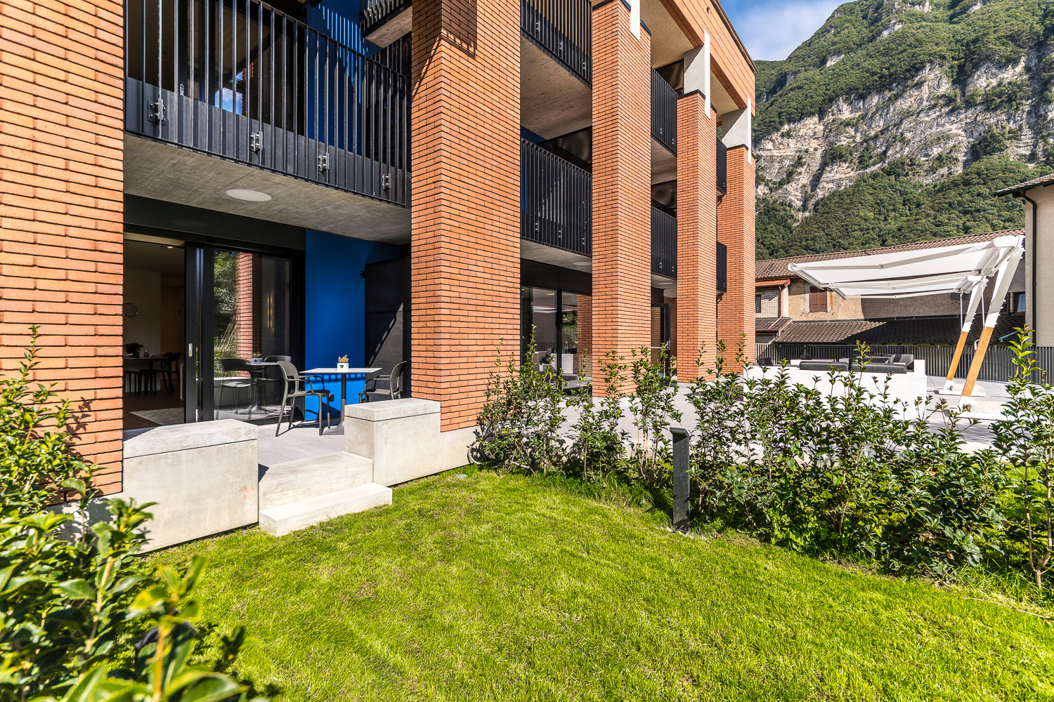 Multi-story apartment building with brick facade, balconies, and outdoor seating area with lawn and landscaping