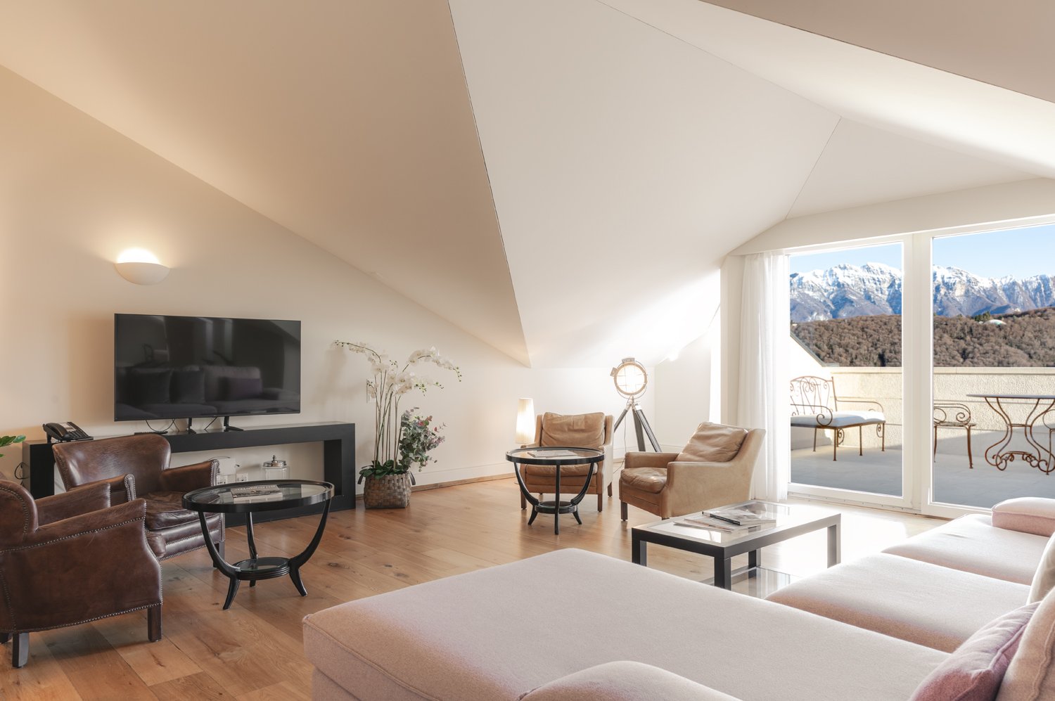 Living room with large glass window, balcony, wooden floor, large sofa, coffee tables, armchairs, television
