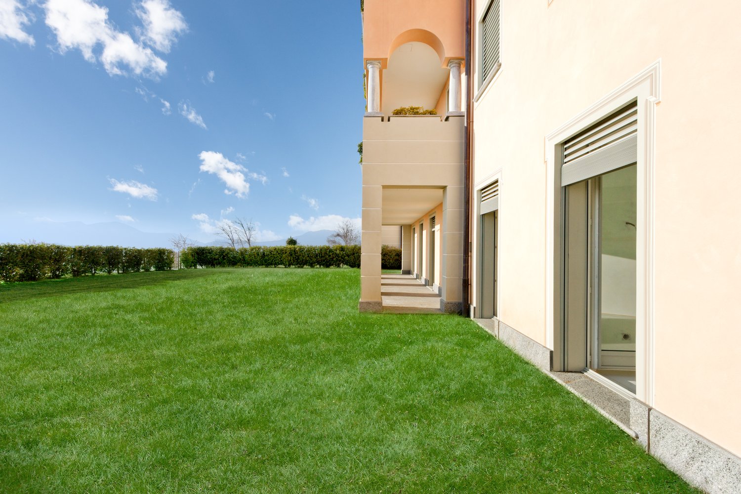 Two-story building with arched entryway, surrounded by a well-manicured lawn and landscaping, with large windows and a balcony or terrace visible.
