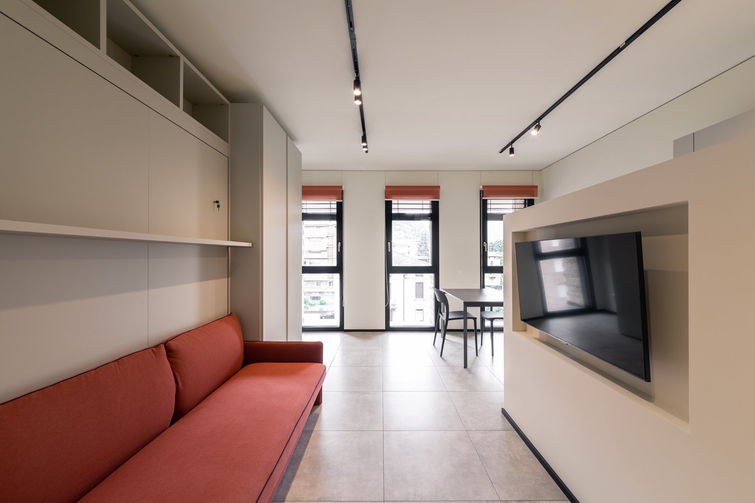 a modern living room with a red sofa, white shelves, a flat-screen TV, and a dining table