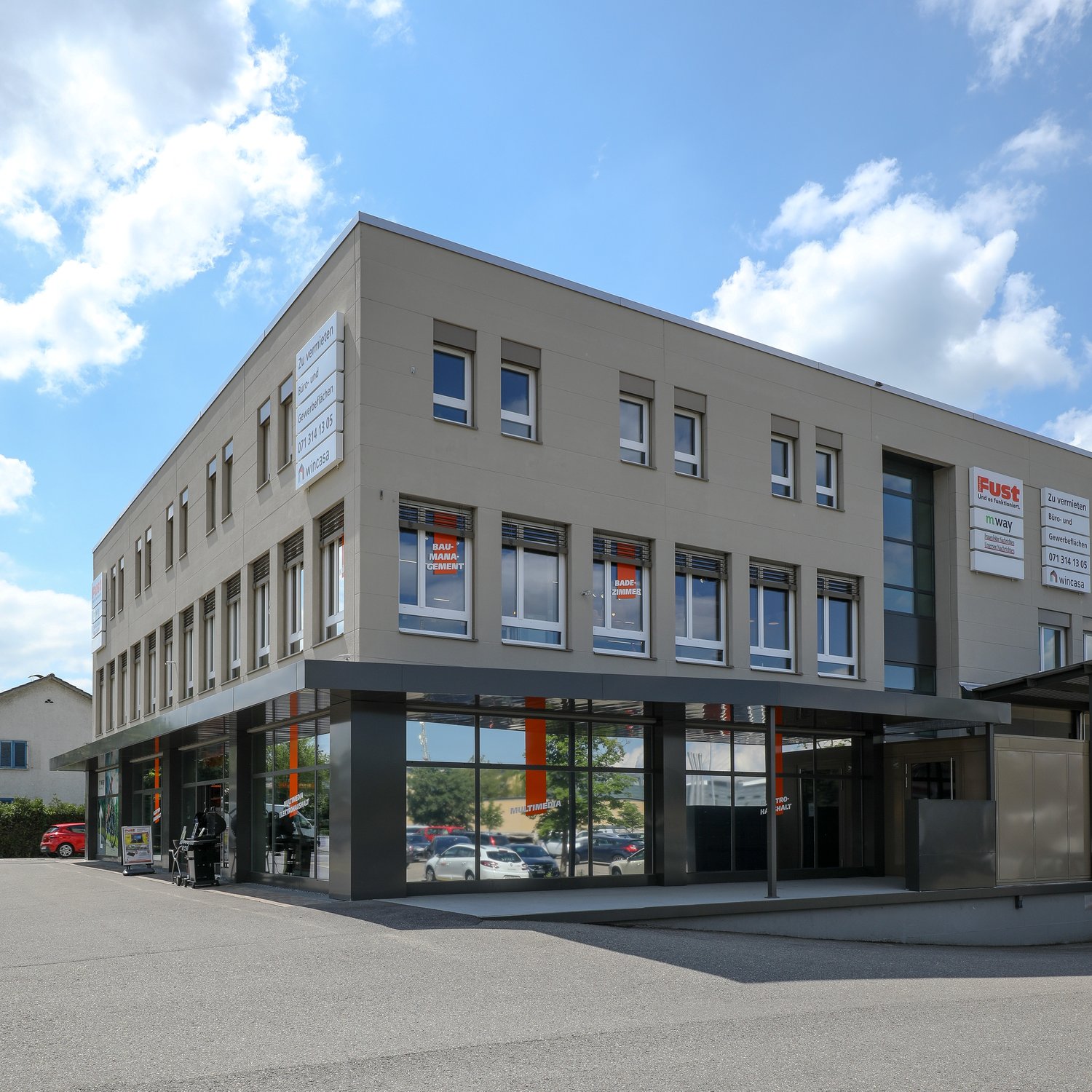 A 3 story building, grey walls, glass windows, signages, cars parked in front