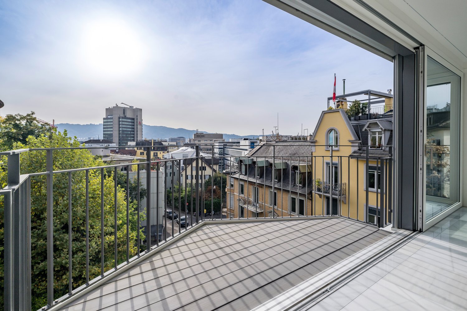 Terrace balcony with railing, tiled flooring, city view with buildings and mountains