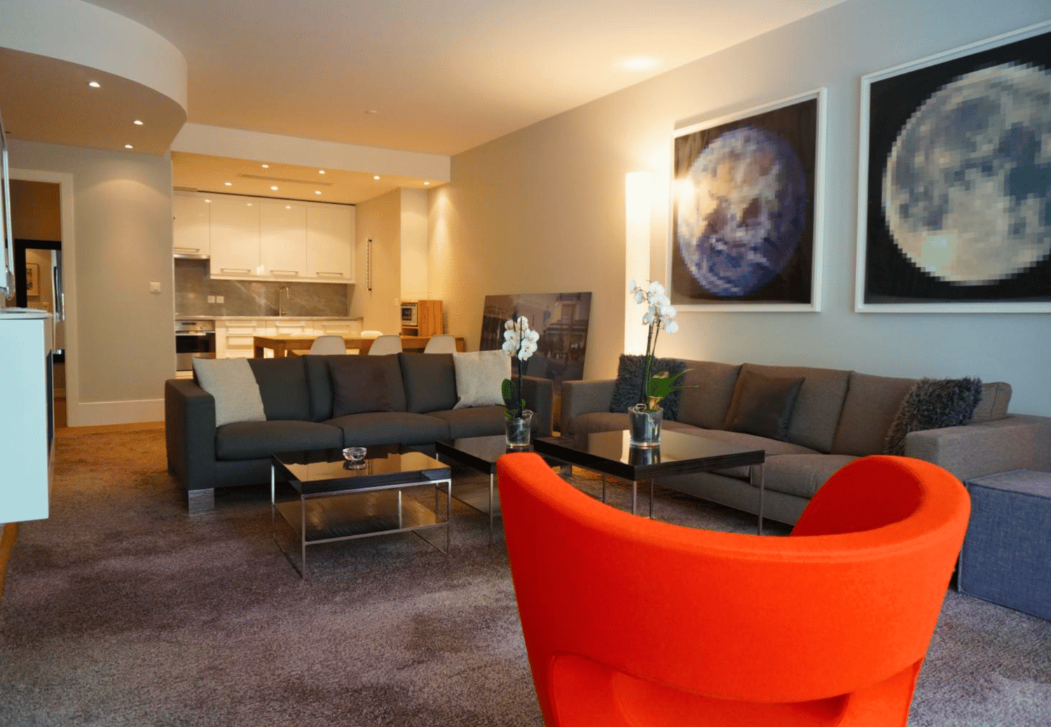 large living area with modern furnishings, 2 grey sofas, glass coffee tables, orange accent chair, large paintings on wall