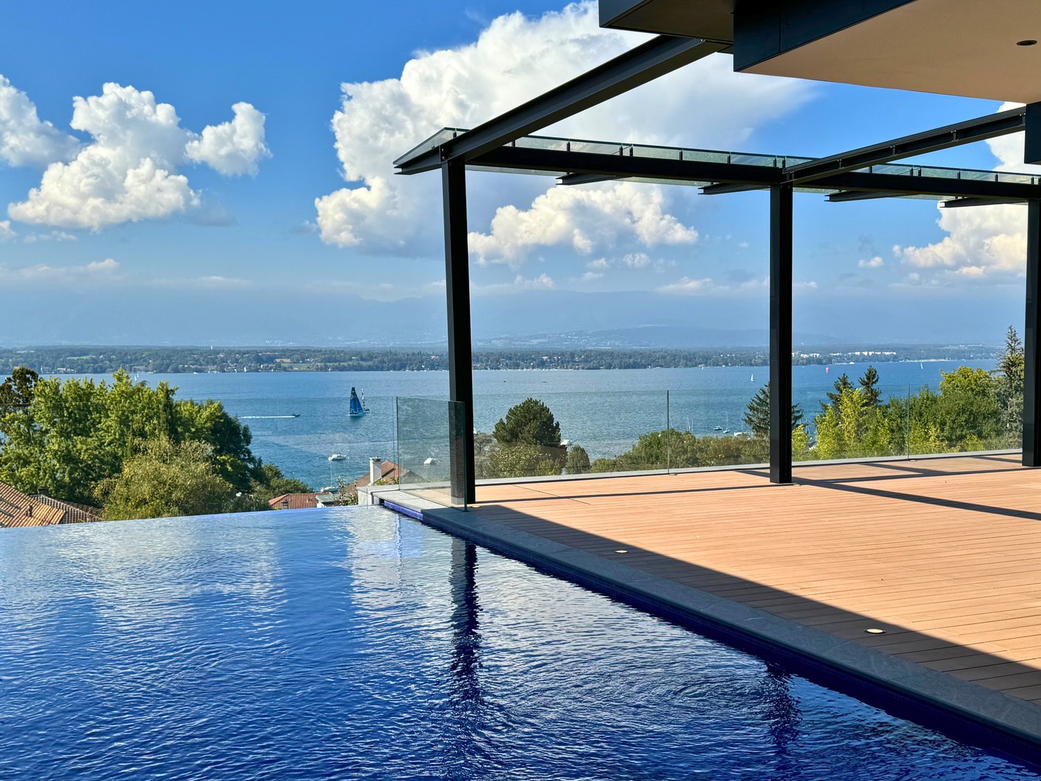 Modern infinity pool with wooden deck, glass railings, clear blue water, ocean view