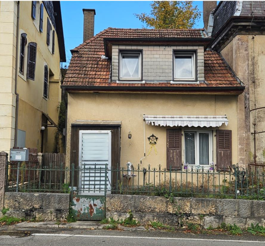 House with red tiled roof, brown and yellow walls, black-framed windows, white doors, green iron fence, garage
